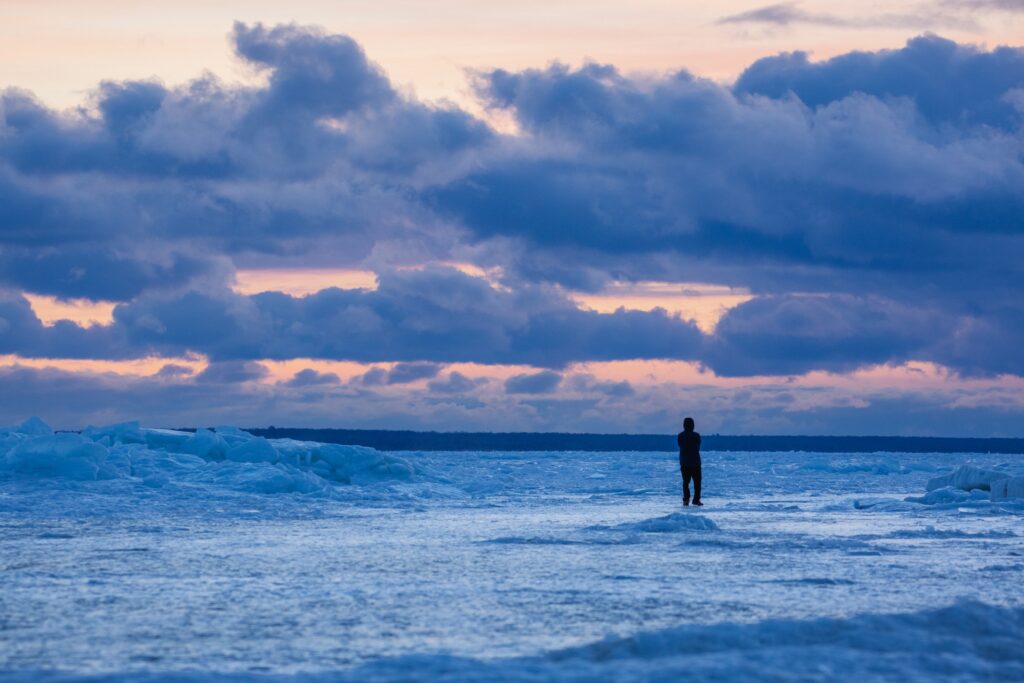 Man watches sunrise on frozen Lake Huron.
