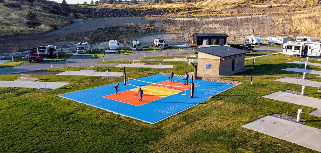 Guests playing pickleball at Klamath Falls RV Park on a sunny day, with paddles in hand and a scenic mountain backdrop.
