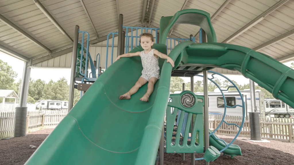 A child happily goes down a green slide at the covered playground at Lakeside RV Resort by RJourney